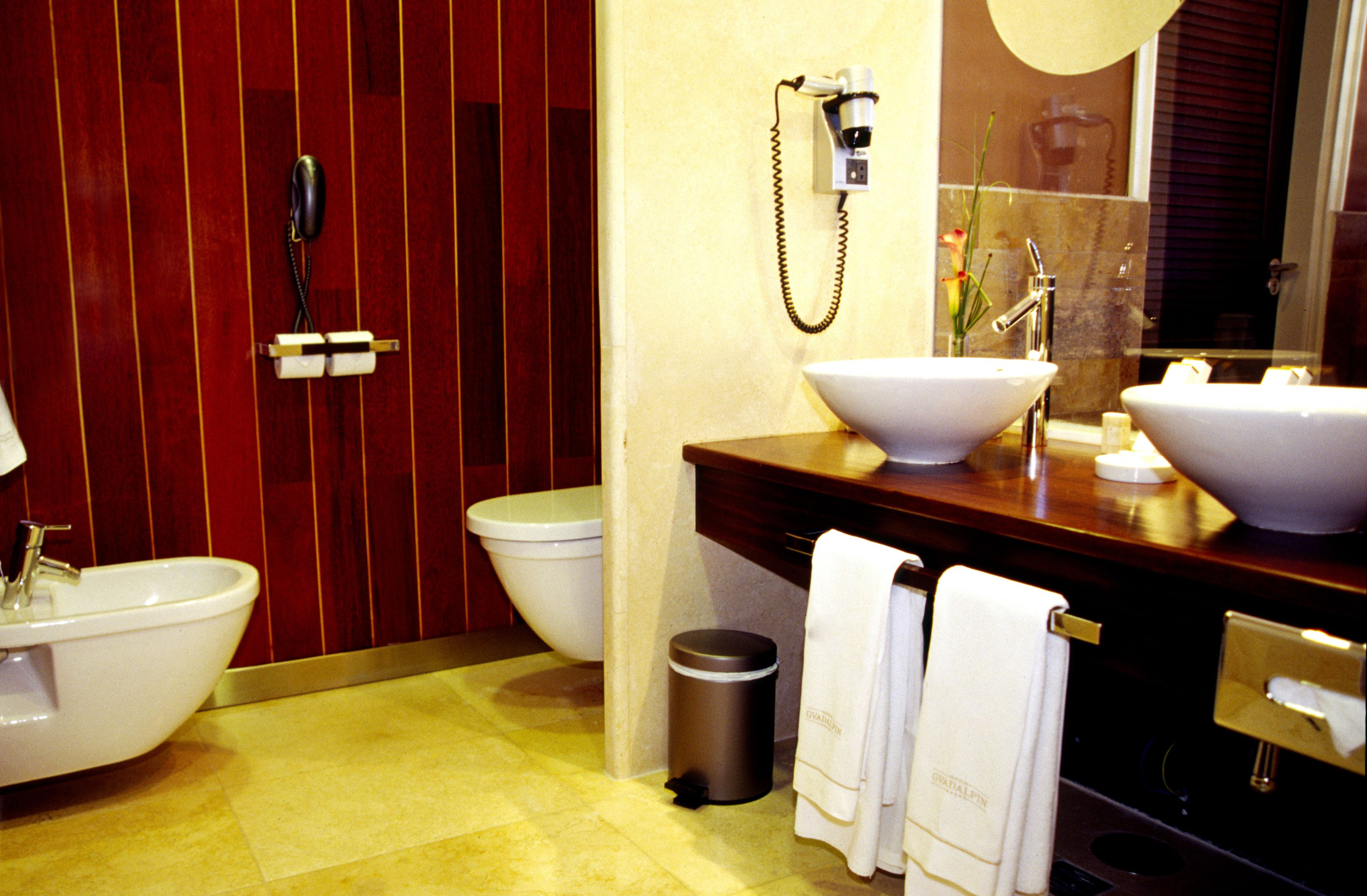 A bathroom with a wooden vanity, two sinks, a toilet, a trash can, and a towel rack.