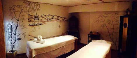 A room with two beds, a wall mural, a small table with a bottle, and a decorative tree branch.