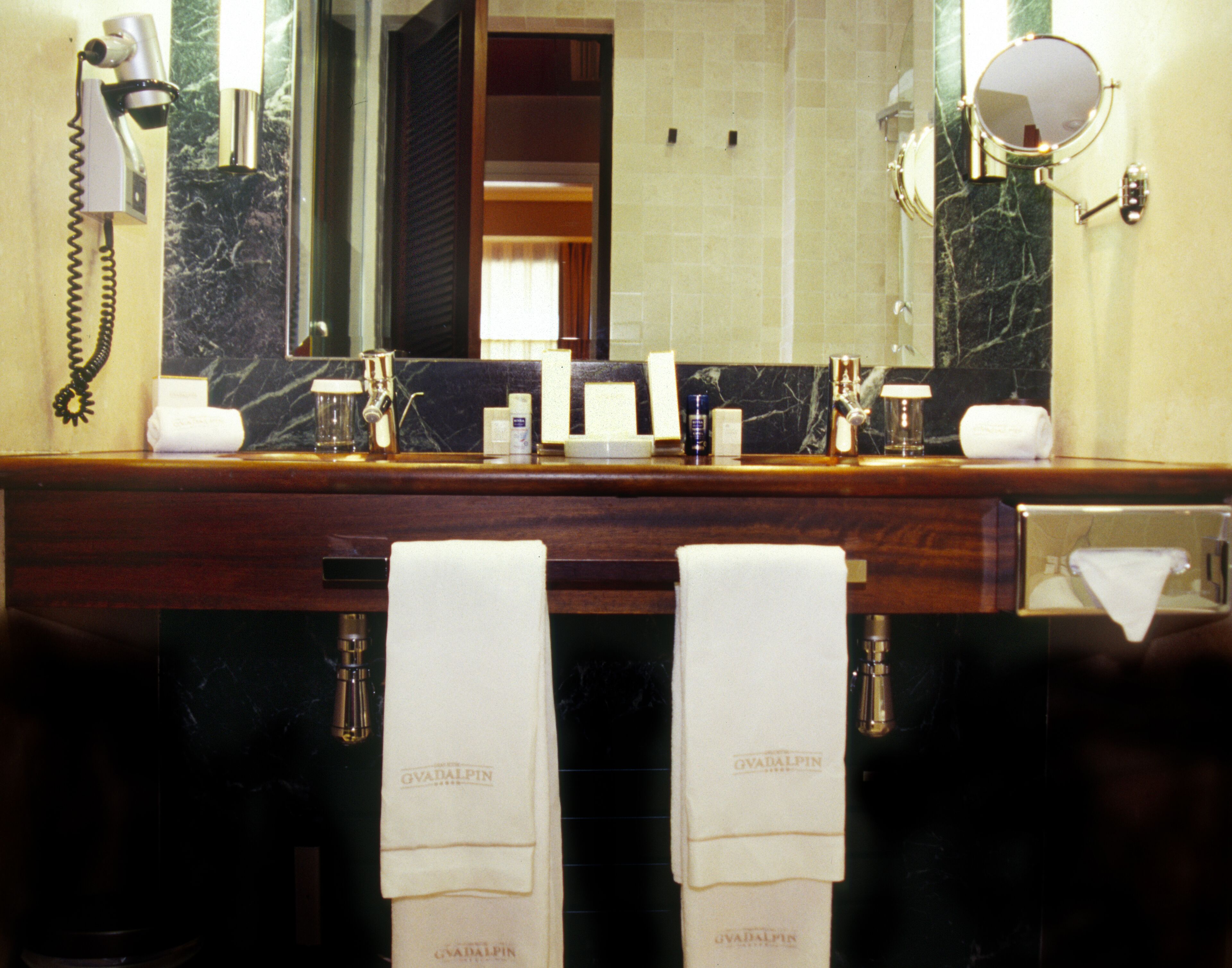 A bathroom with a marble countertop, a hairdryer, a mirror, and two towels hanging on the wall.