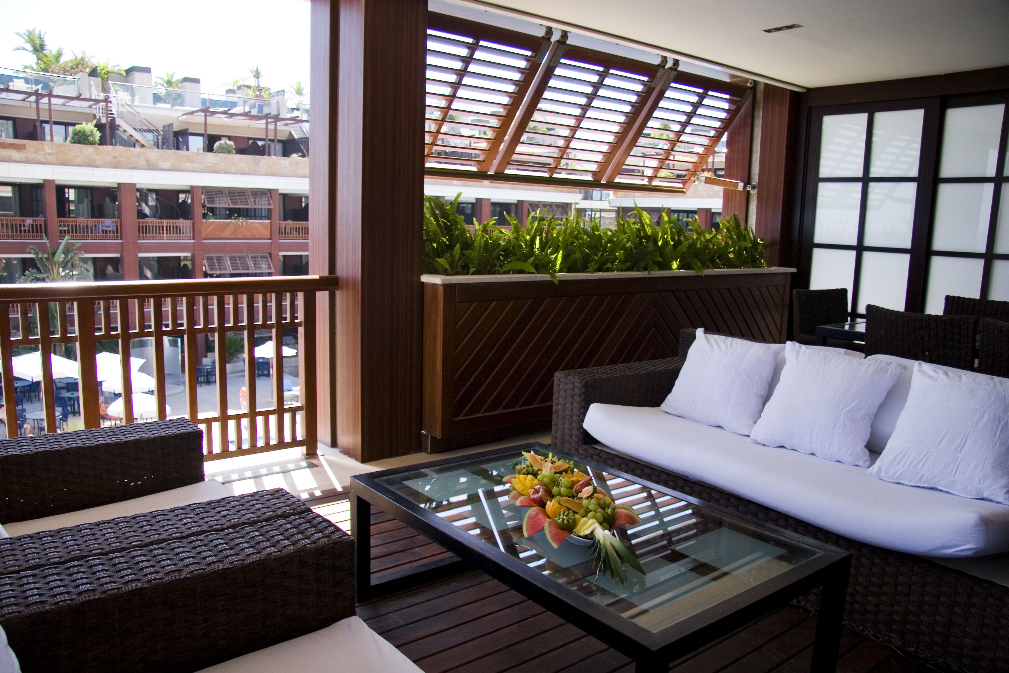 A balcony with a sofa, a glass coffee table with fruit, and a view of buildings.