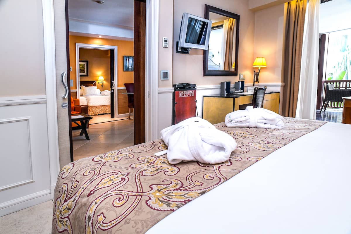 A hotel room with a large bed, a television mounted on the wall, a desk with a chair, and a view of the outside through a window.