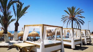 A beachside resort with thatched umbrellas, wooden beds with white curtains, and palm trees. - Gran Hotel Guadalpin Banus (Marbella)