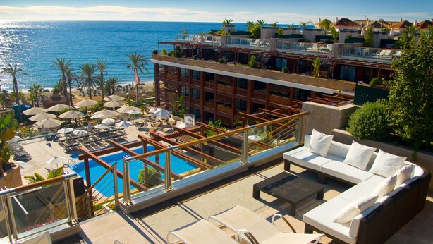 A rooftop pool area with lounge chairs and a sofa, overlooking a beach and the sea.