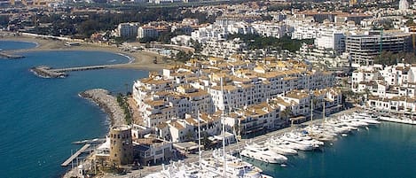 An aerial view of a coastal city with a marina, buildings, and mountains in the background.