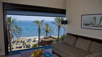 Una habitación con un ventanal grande con vista a una playa, un sofá estampado y una mesita con un jarrón.