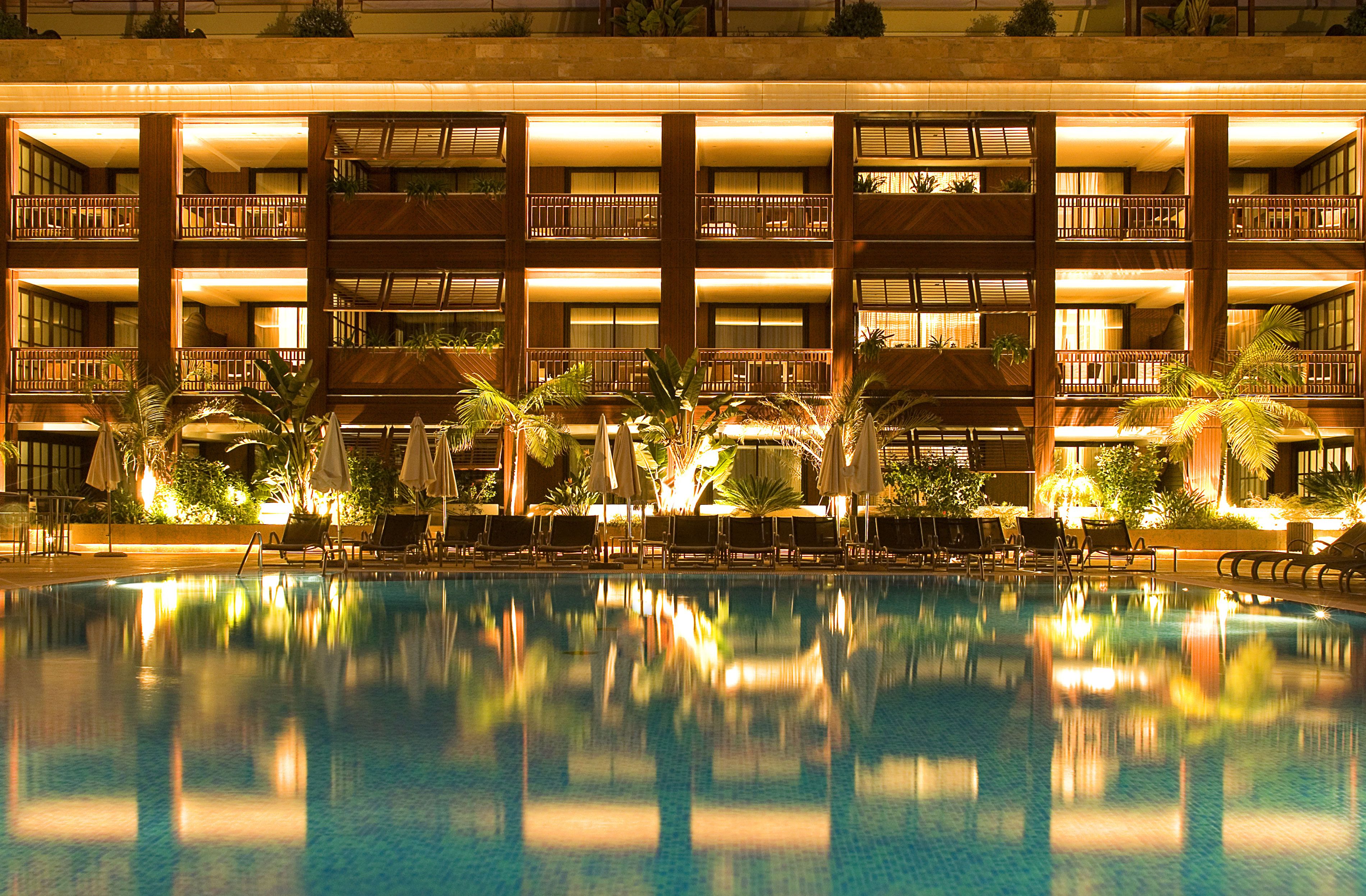 Un hotel con una amplia piscina cubierta, varios balcones y zonas de estar exteriores con sombrillas.