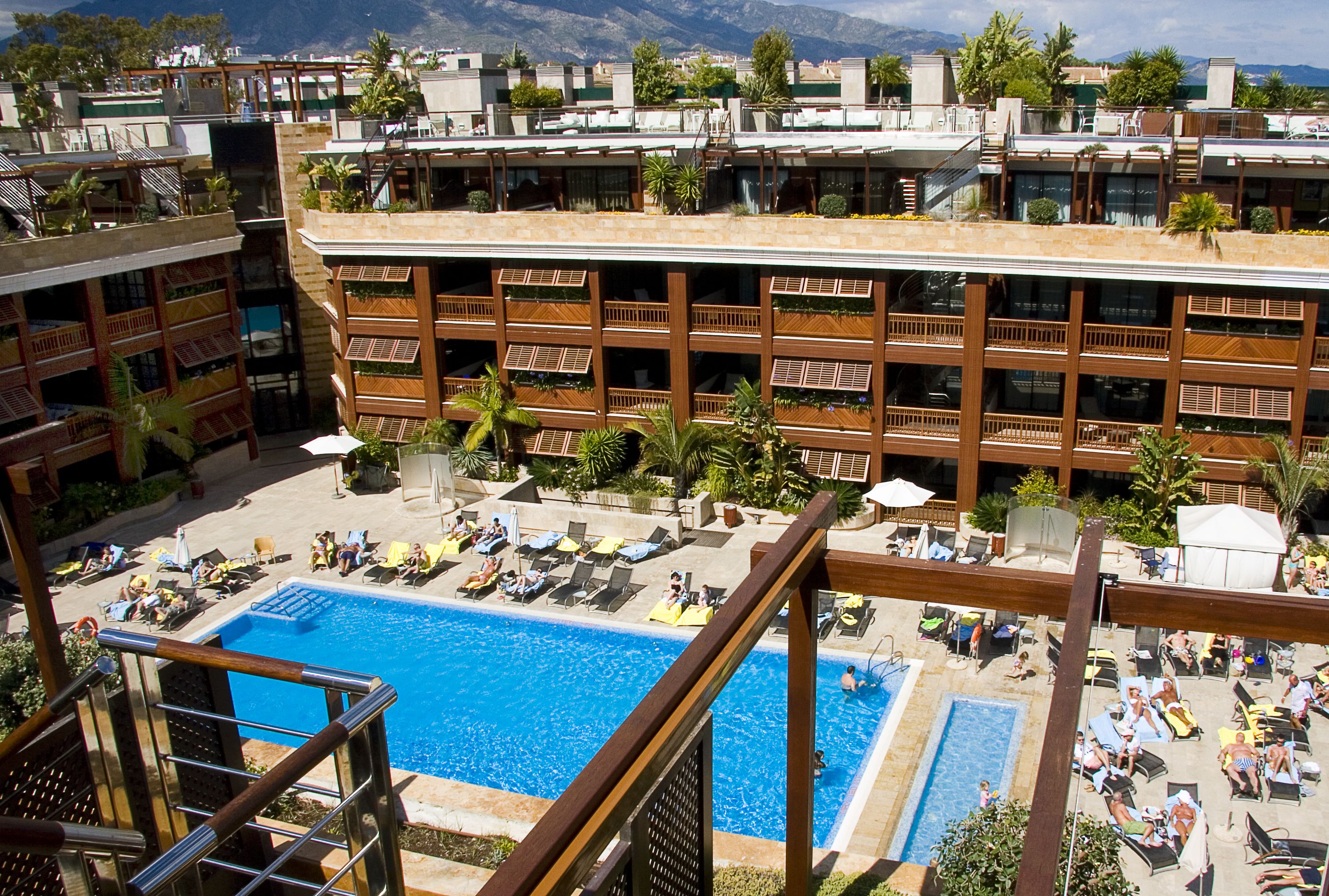 Un hotel con varios balcones, una piscina central y tumbonas.