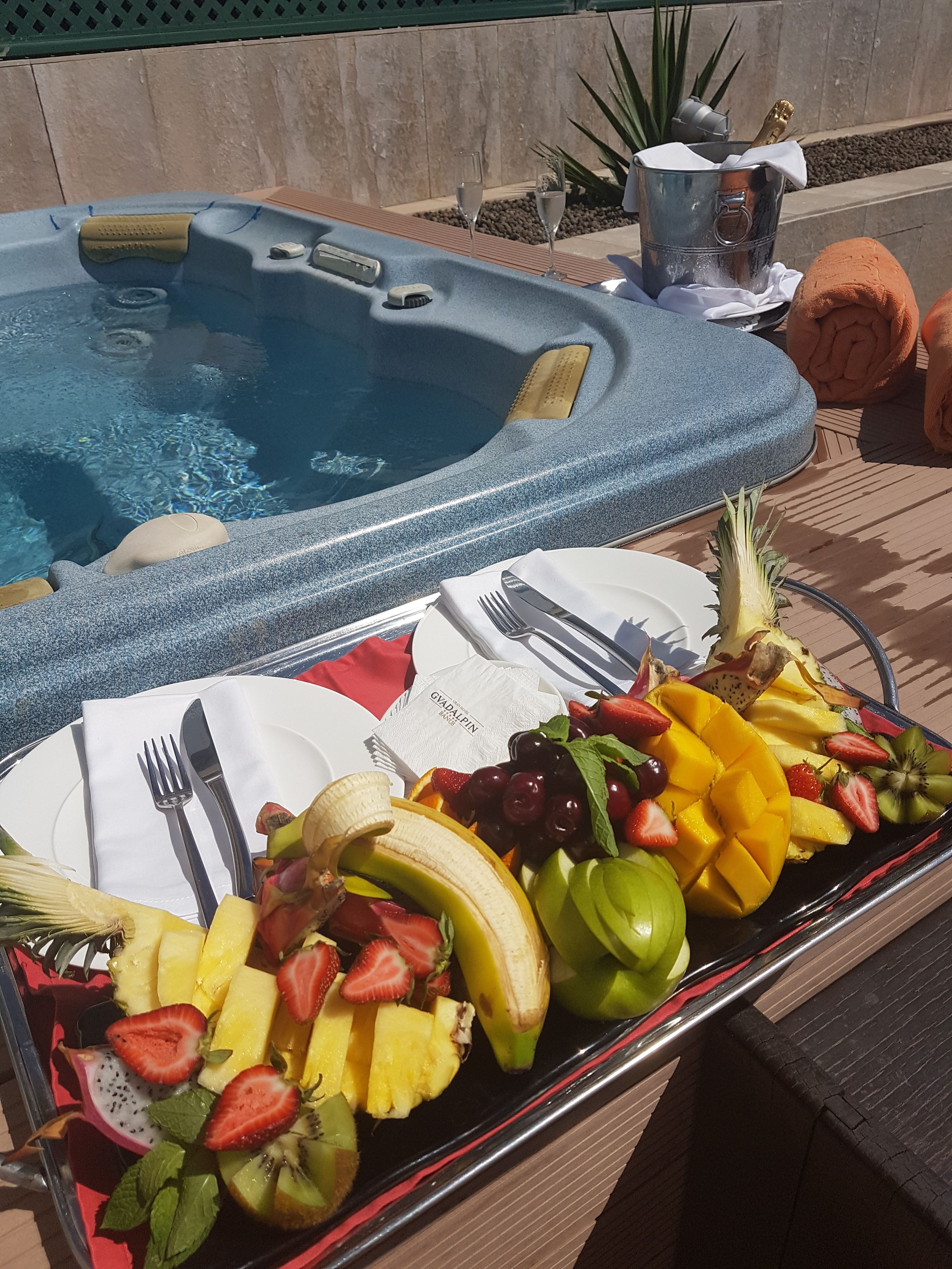 Un bain à remous avec une table placée au bord de la piscine, dressée pour un repas comprenant des fruits et une boisson.