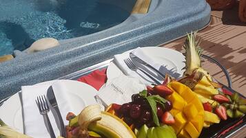 Un bain à remous avec une table placée au bord de la piscine, dressée pour un repas comprenant des fruits et une boisson.