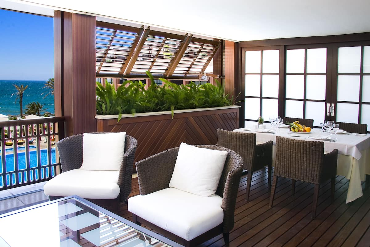 A balcony with wicker chairs, a dining table set for two, and a view of the ocean.