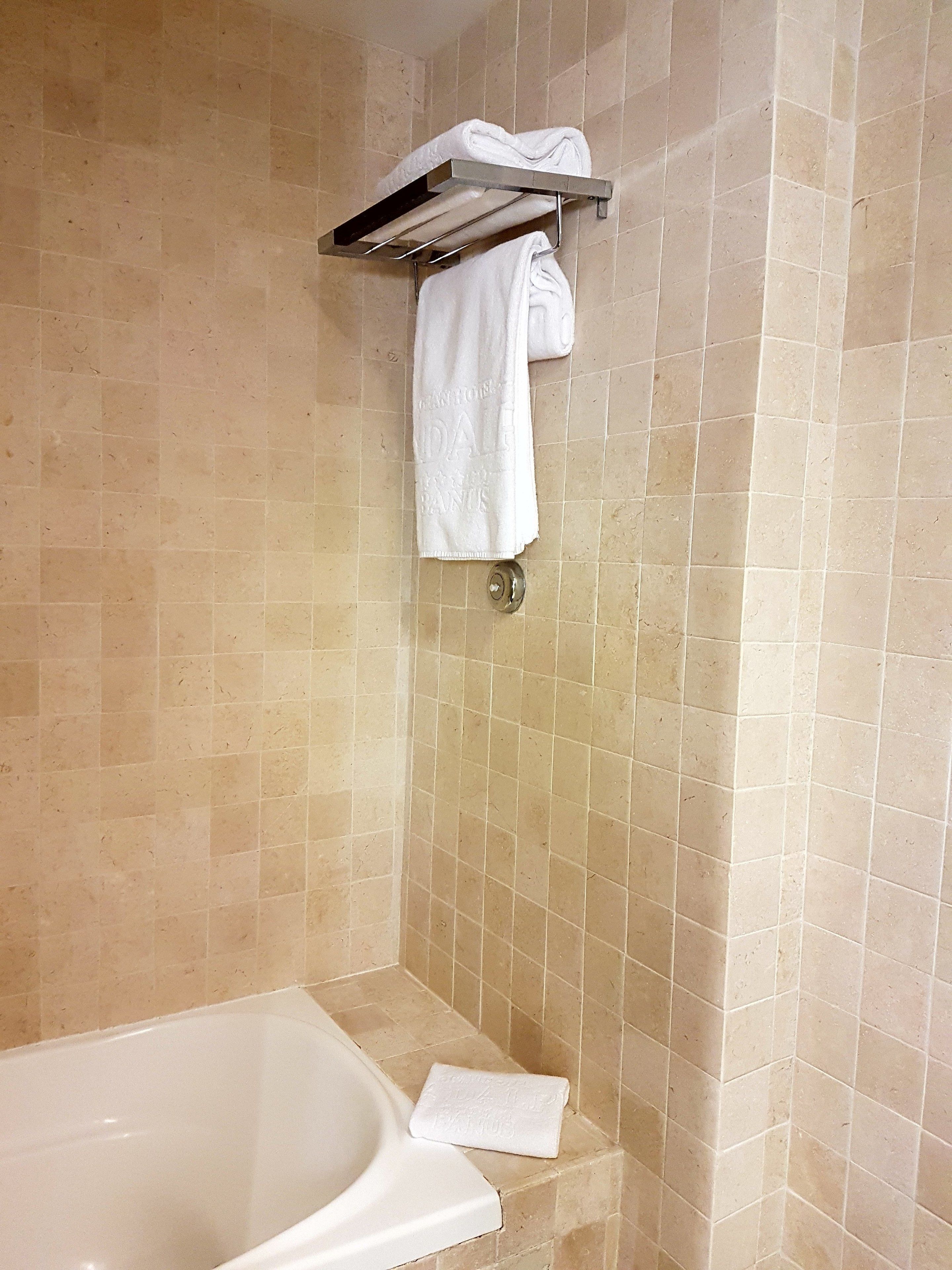 Ein Badezimmer mit einer Badewanne, einem Handtuchhalter mit zwei Handtüchern und beige gefliesten Wänden.