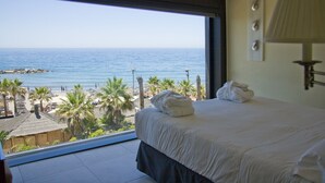 A hotel room with a large window offering a view of the beach and ocean.
