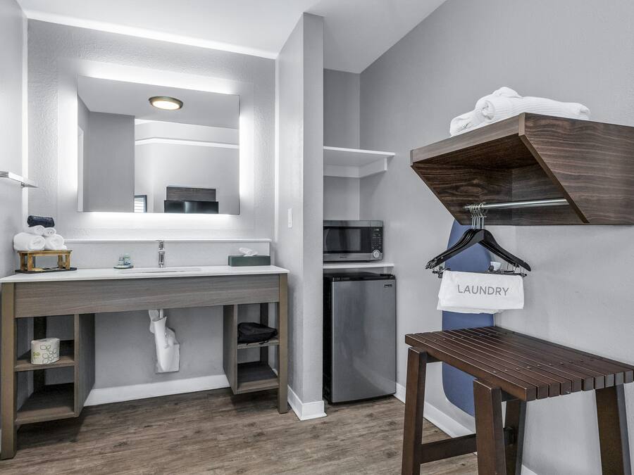 A modern bathroom with a large mirror, built-in sink, and a compact refrigerator.