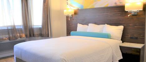 A hotel room with a large bed, a nightstand, a wall-mounted lamp, and a window with curtains.