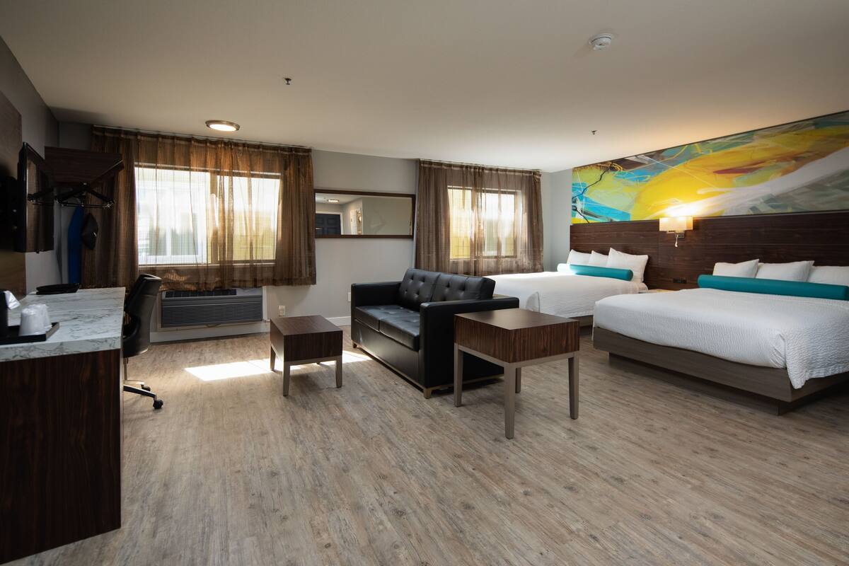 A hotel room with a bed, a sofa, a desk, and a large painting on the wall.