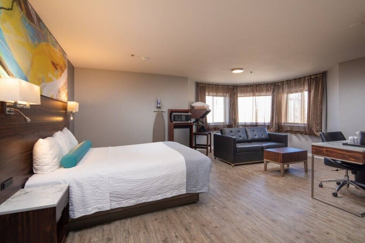 A hotel room with a bed, a desk, a sofa, and a large window with curtains.