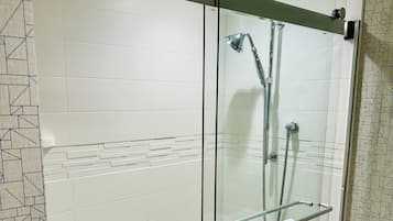 A glass-enclosed shower stall with a glass door, a towel rack with a towel, and a showerhead.