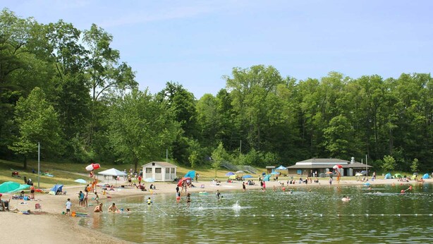 A lakeside beach with tents, a pavilion, and people swimming and relaxing. - Holiday Inn Express & Suites Milton by IHG (Milton)