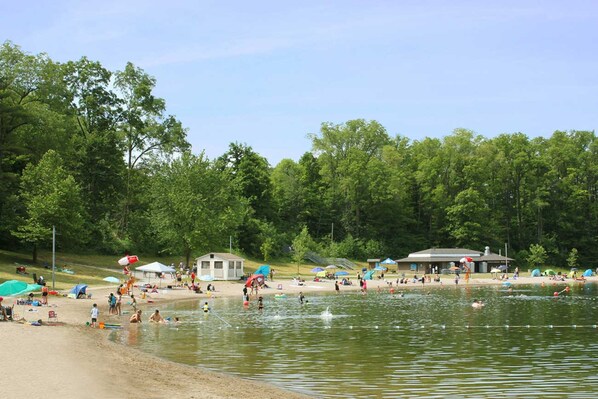 A lakeside beach with tents, a pavilion, and people swimming and relaxing. - Holiday Inn Express & Suites Milton by IHG (Milton)