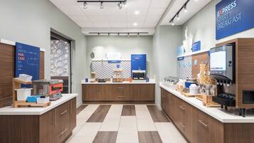 A modern breakfast area with a bakery counter, a coffee station, and a self-serve beverage dispenser.
