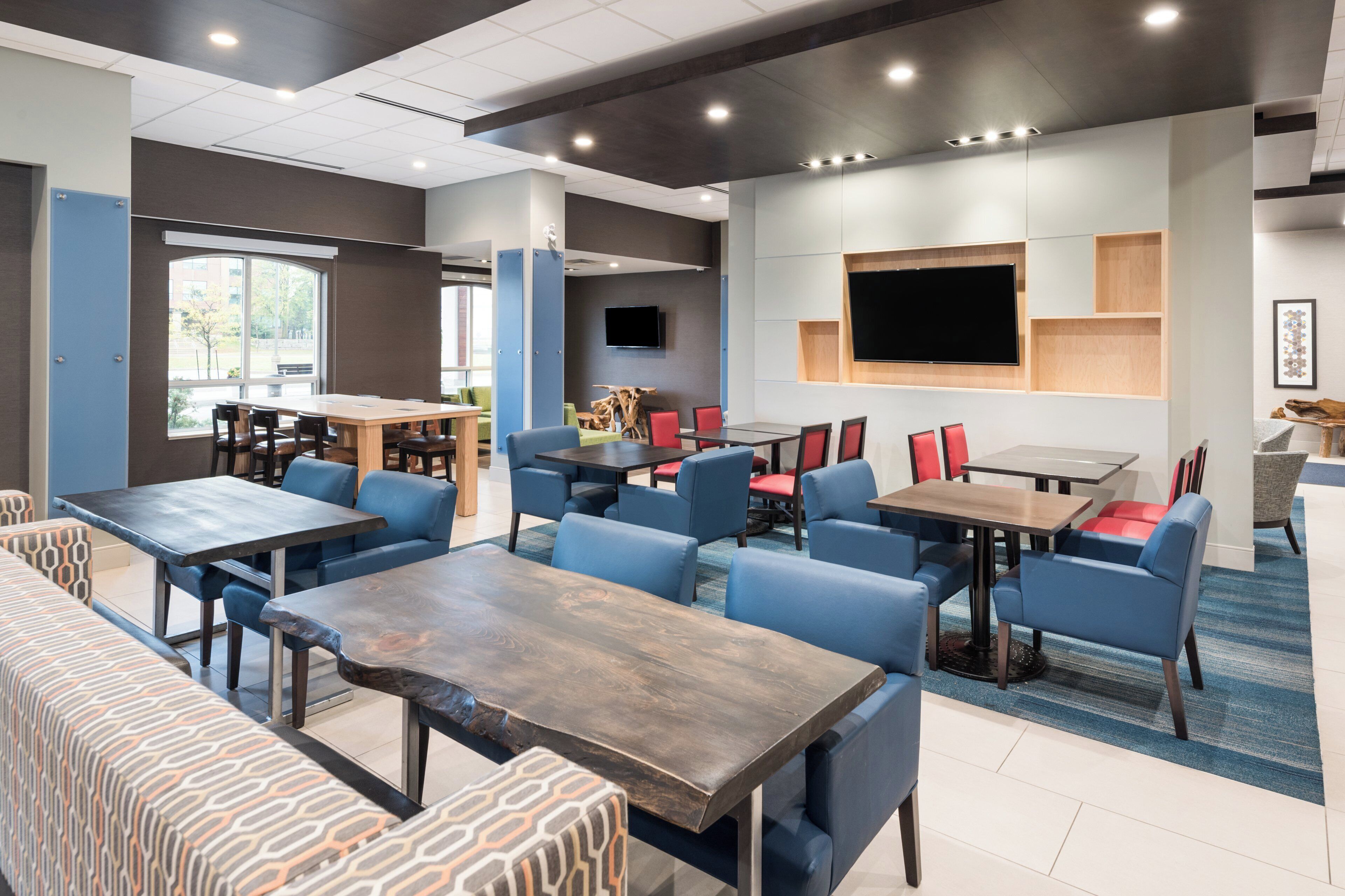 A modern indoor space with multiple seating areas, including tables and chairs, and a flat-screen TV mounted on the wall.