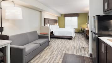 Une chambre d’hôtel avec un lit, un canapé, un bureau, un réfrigérateur et une fenêtre.