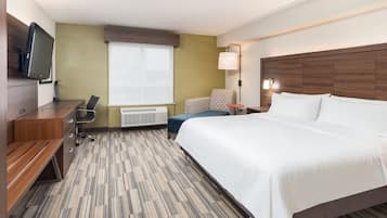 A hotel room with a large bed, a desk with a chair, a television, and a window with blinds.