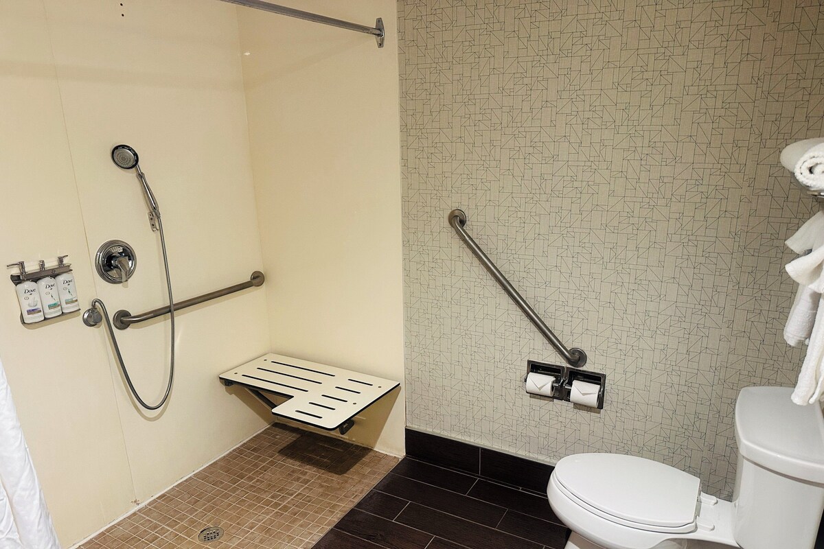 A bathroom with a shower, toilet, grab bars, and a towel rack.