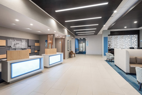 A modern hotel lobby with a reception desk, a blue exit sign, and a patterned wall. - Holiday Inn Express & Suites Milton by IHG (Milton)