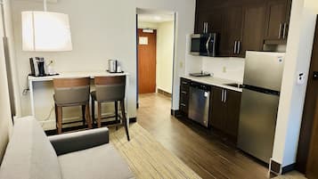 Una habitación de hotel compacta con kitchenette, sofá, cafetera y microondas.
