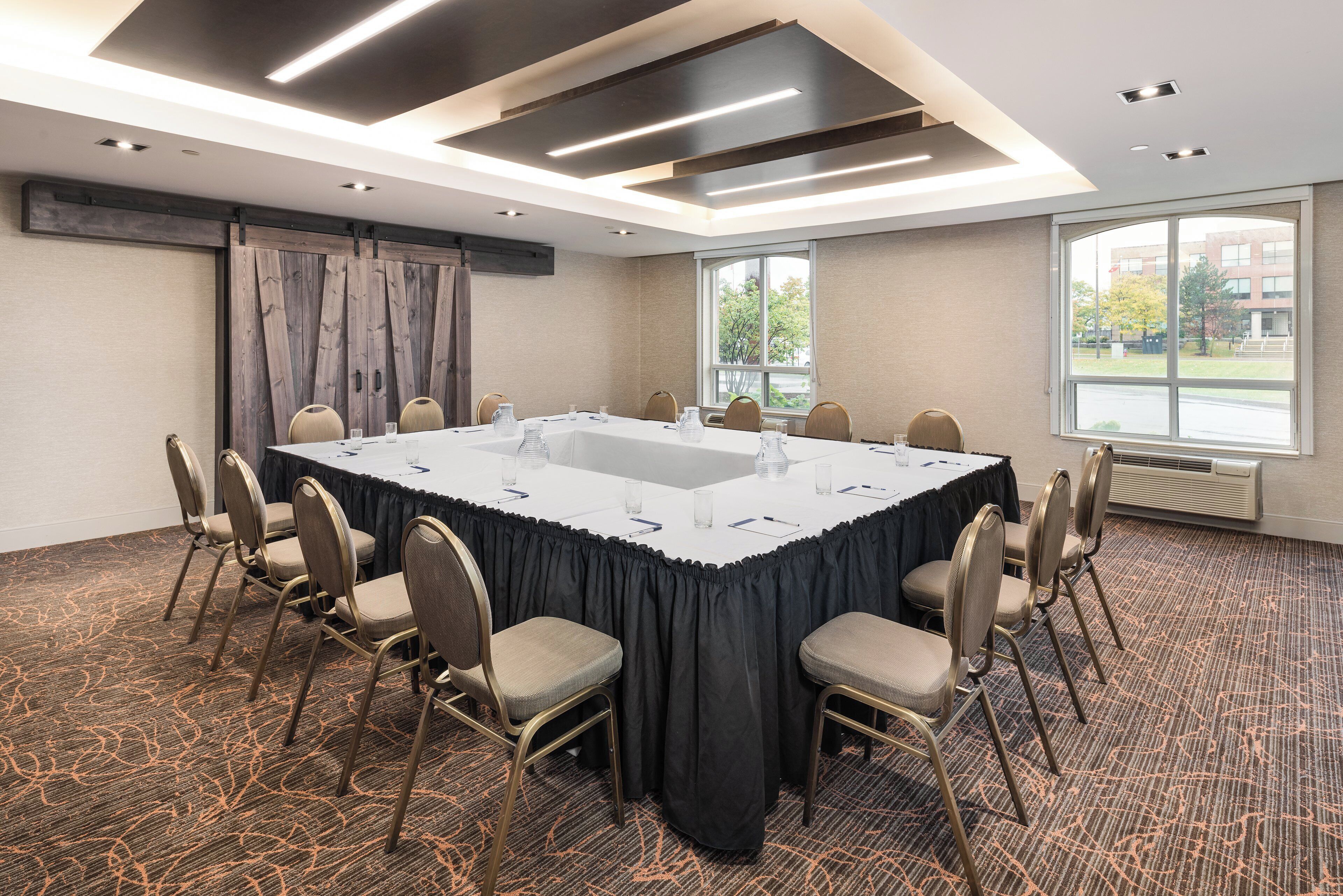A conference room with a large table, chairs, and a view of the outdoors through a window.