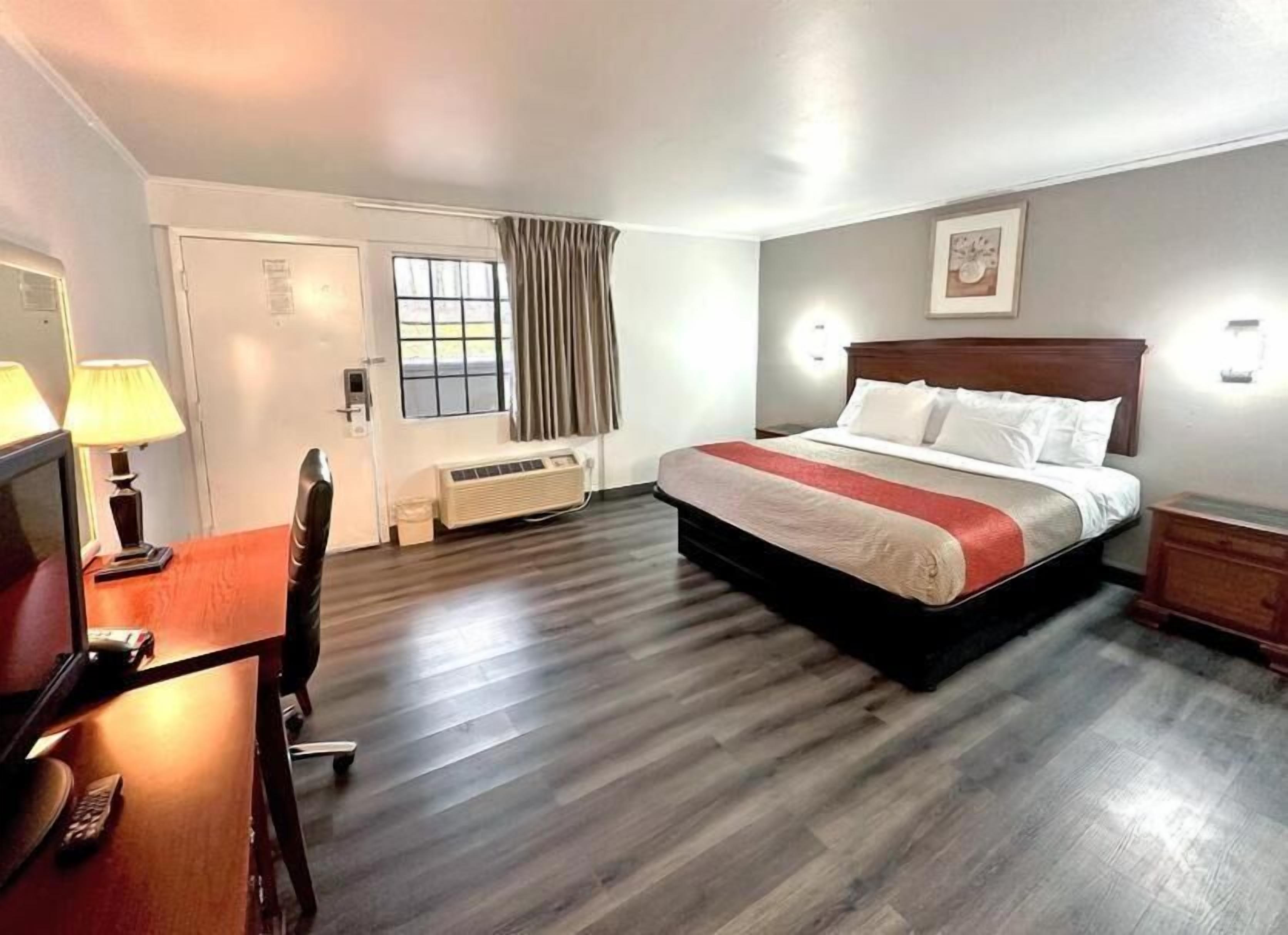 A hotel room with a bed, desk, chair, and a window with curtains.
