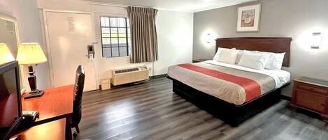 A hotel room with a bed, desk, chair, and a window with curtains.