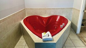Una bañera con forma de corazón, con una toalla y artículos de aseo a un lado.