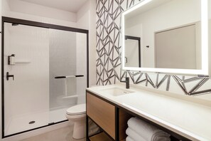 Un baño moderno con ducha envuelta en vidrio, inodoro blanco, tocador con espejo y pared con diseño.
