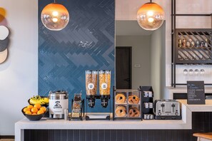 A breakfast bar with a coffee machine, a bowl of oranges, and a sign listing available food items. - Atwell Suites Panama City Beach Southeast by IHG (Panama City Beach)