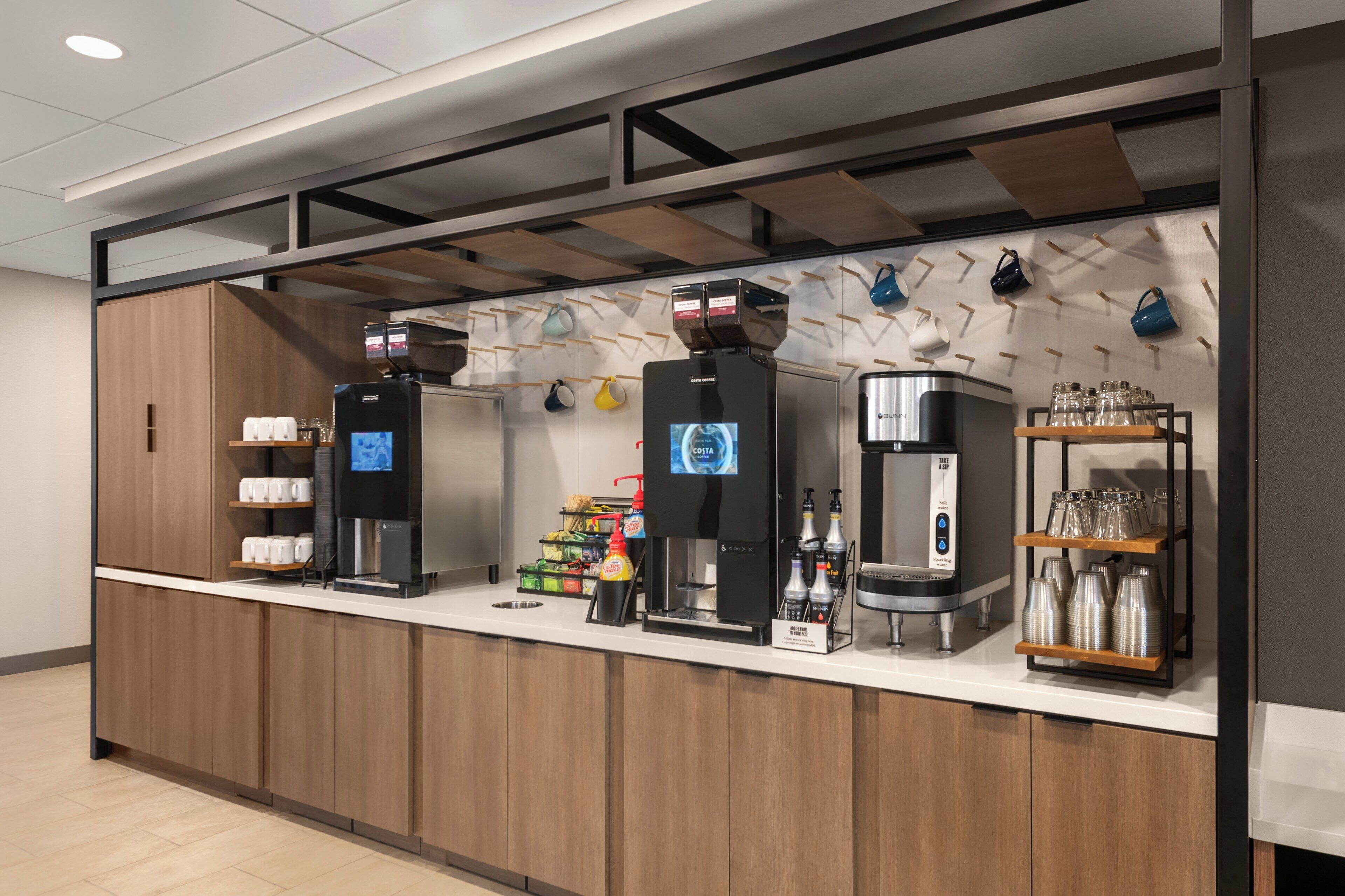 A coffee station with multiple coffee machines, a water dispenser, and a variety of coffee cups and mugs displayed on shelves.