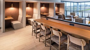 Una habitación de hotel moderna con una larga mesa de madera, varios taburetes de bar y un amplio ventanal con vistas a la ciudad.