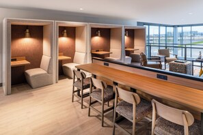 Una habitación de hotel moderna con una larga mesa de madera, varios taburetes de bar y un amplio ventanal con vistas a la ciudad.