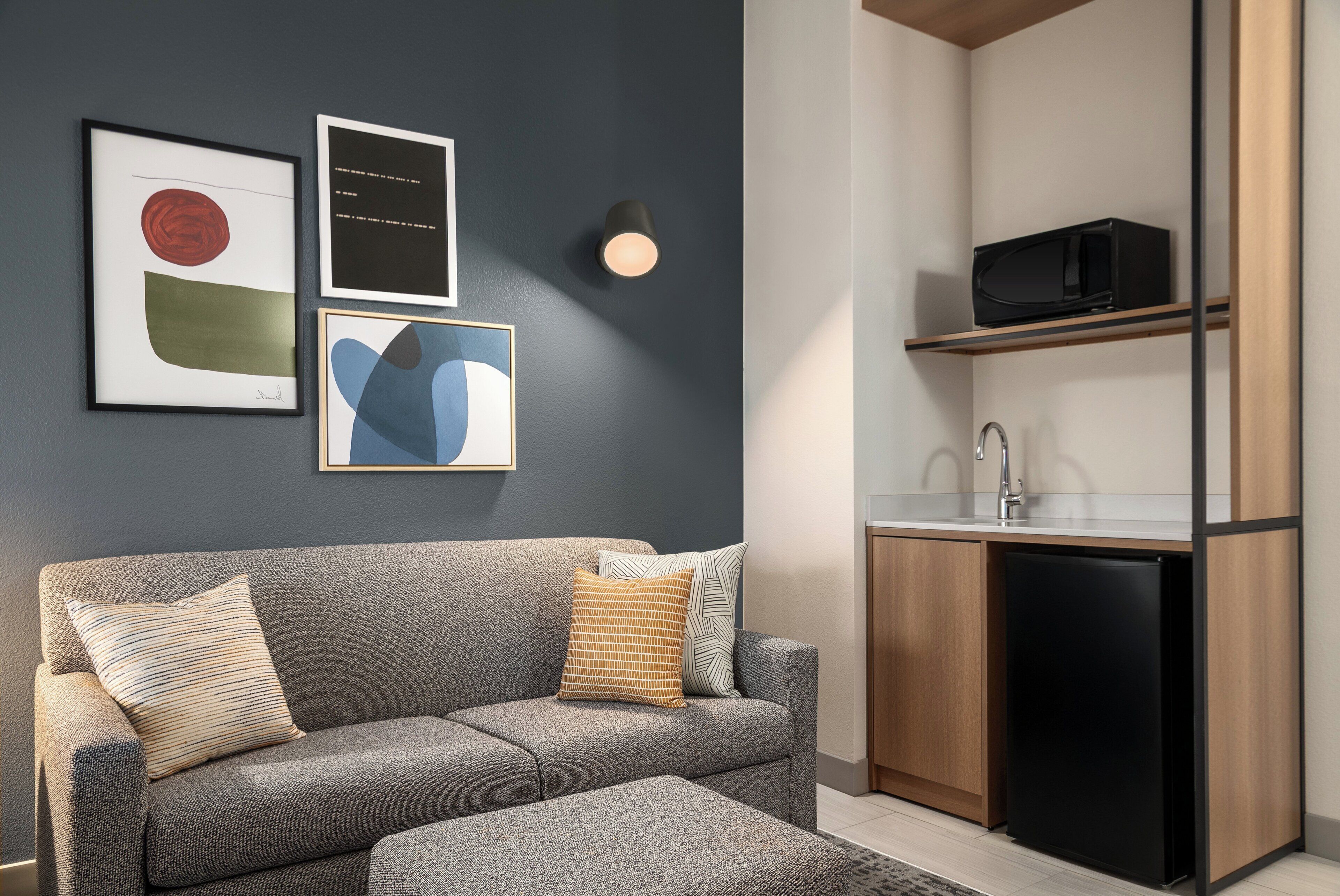 En moderne stue med en grå sofa, et sofabord og et køkken med mikroovn og vask.