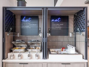 Ein Frühstücksbuffet mit ausgeschilderten warmen und kalten Speisen, darunter Rührei, Omelett mit Eiklar und Gemüse sowie Milch.