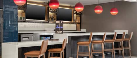 Zona de bar moderna con mostrador, taburetes y lámparas colgantes rojas.