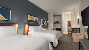 A hotel room with two beds, a desk, a chair, a television, and artwork on the walls.