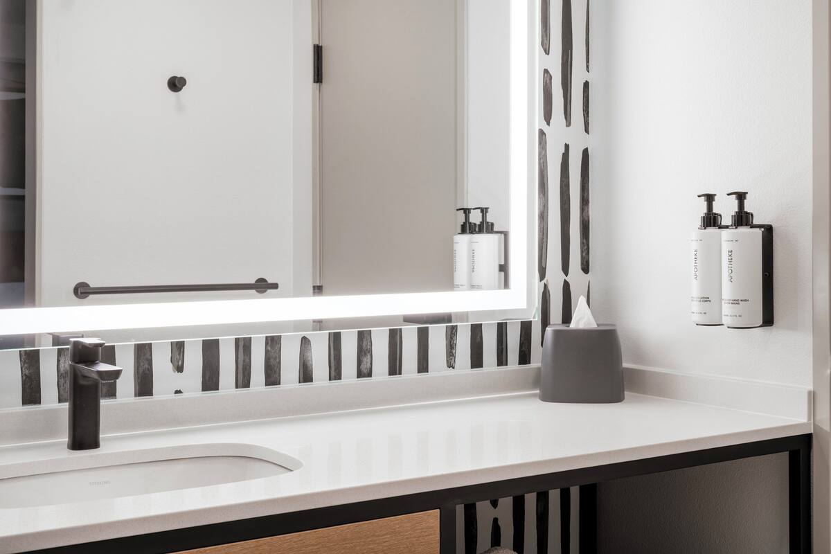 Une salle de bain moderne avec un lavabo blanc, un grand miroir et des produits de toilette fixés au mur.