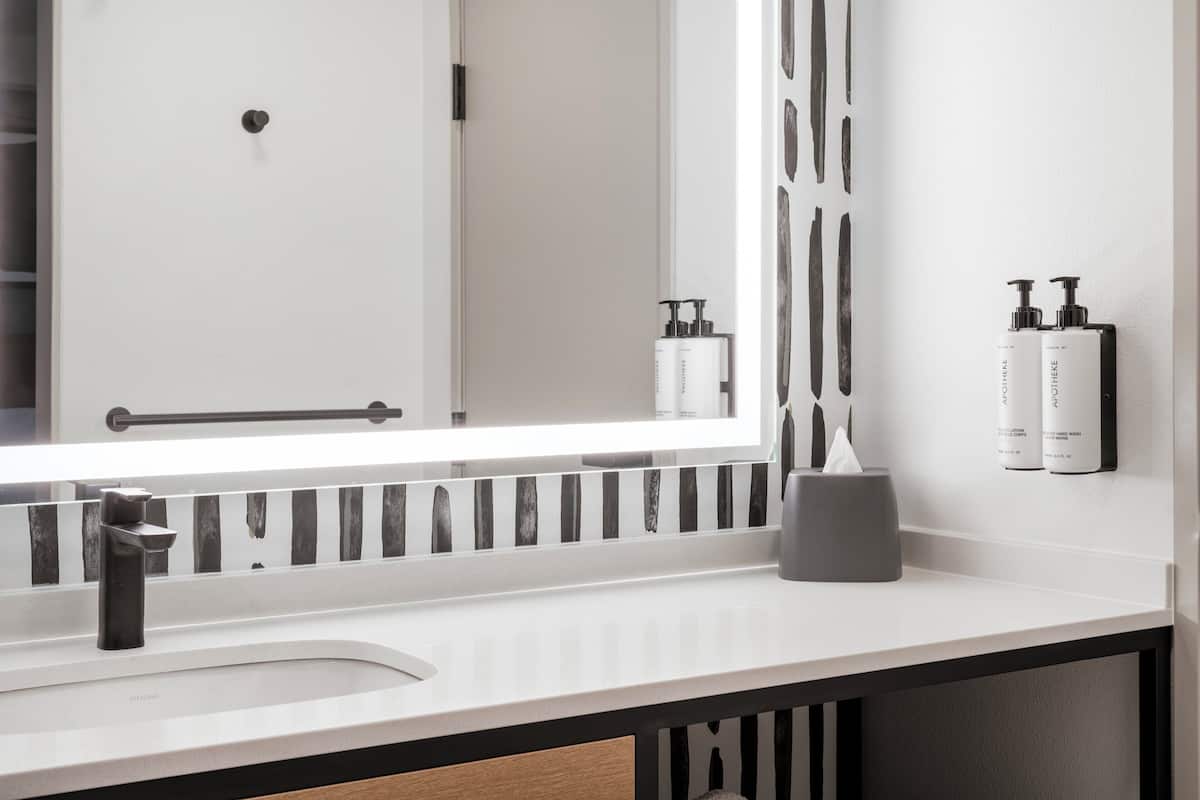 A modern bathroom with a white sink, a large mirror, and toiletries on the wall.