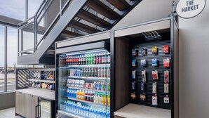Zona de máquinas expendedoras con diversas bebidas y aperitivos, un expositor refrigerado y un cartel que dice 'THE MARKET'.