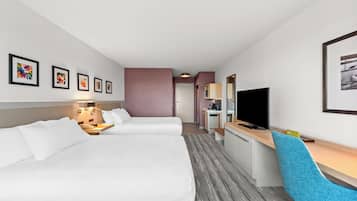 Habitación de hotel con dos camas, un escritorio, una silla, televisión y obras de arte en las paredes.