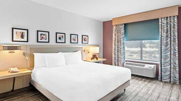Ein Hotelzimmer mit einem großen Bett, einem Nachttisch mit Telefon, einer Lampe und einem Fenster mit Vorhängen.