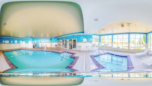 Una amplia piscina interior con solárium de azulejos, sillas de descanso y vistas al exterior a través de grandes ventanales.
