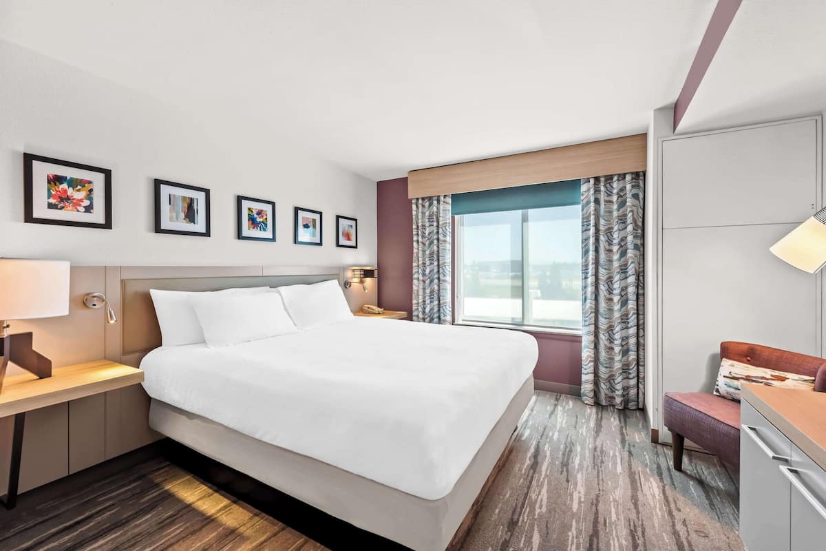 A hotel room with a large bed, bedside tables, a desk, and a view of the city.